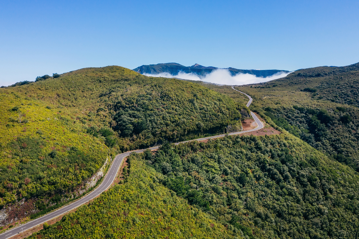 Country asphalt road ER209 leading to clouds stuck at mountain hills in the inland of Madeira island, Portugal aerial drone shot. Traveling and transportation concept image.